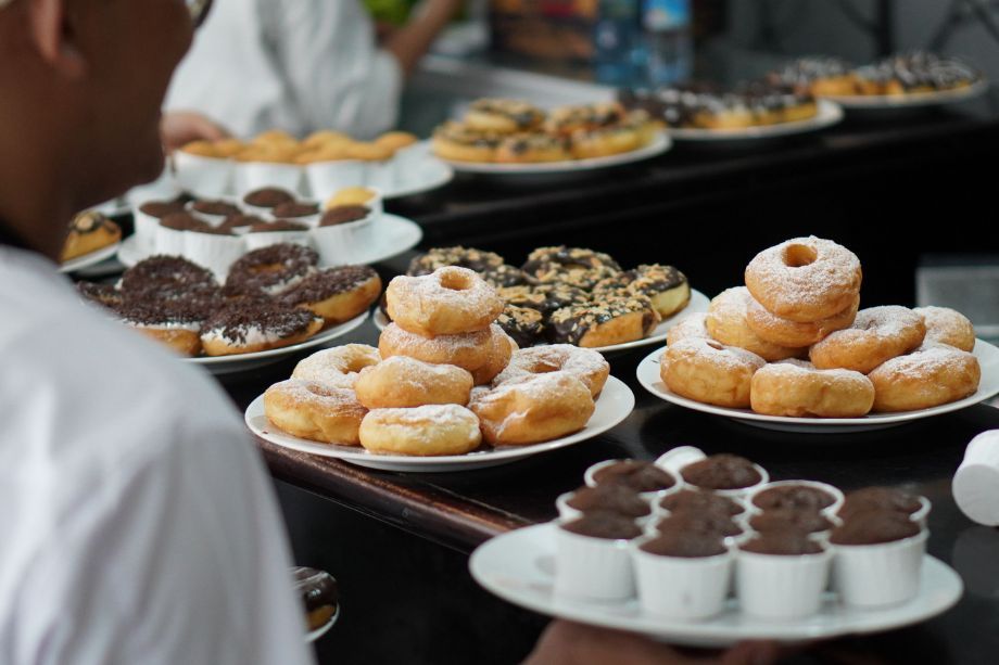 A buffet table with plates of donuts and chocolate pastries, with a person serving in the foreground.