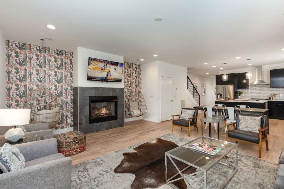 Open-concept living room with a fireplace, wall-mounted TV, and a kitchen island in the background.